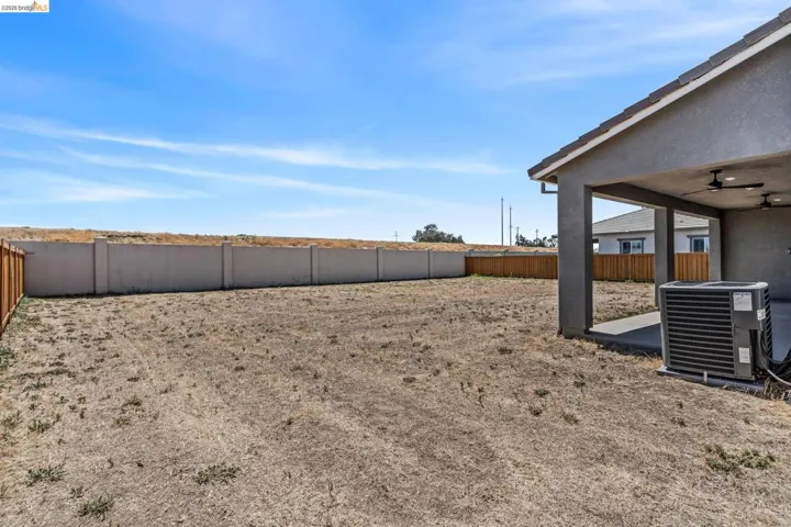 Expansive backyard featuring a concrete patio with an overhead cover, two ceiling fans, and a new privacy fence