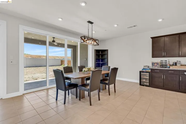 Spacious dining area featuring neutral tile flooring, recessed lighting, and a contemporary linear chandelier