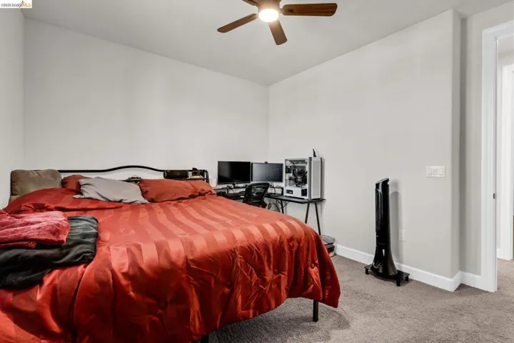 Spacious room featuring neutral painted walls, light-colored carpet flooring, a ceiling fan with integrated lighting, and white baseboards