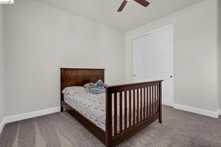 Carpeted bedroom featuring light gray walls, white baseboards, and a ceiling fan with integrated lighting