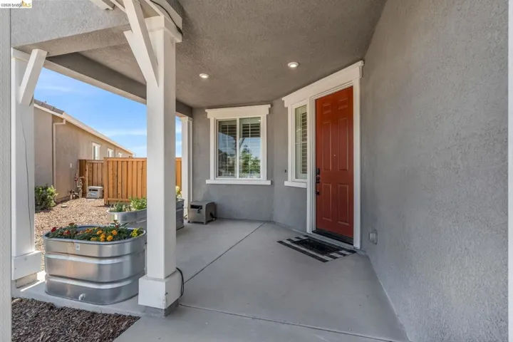 Covered front porch with a red paneled entry door, white trim, and recessed lighting