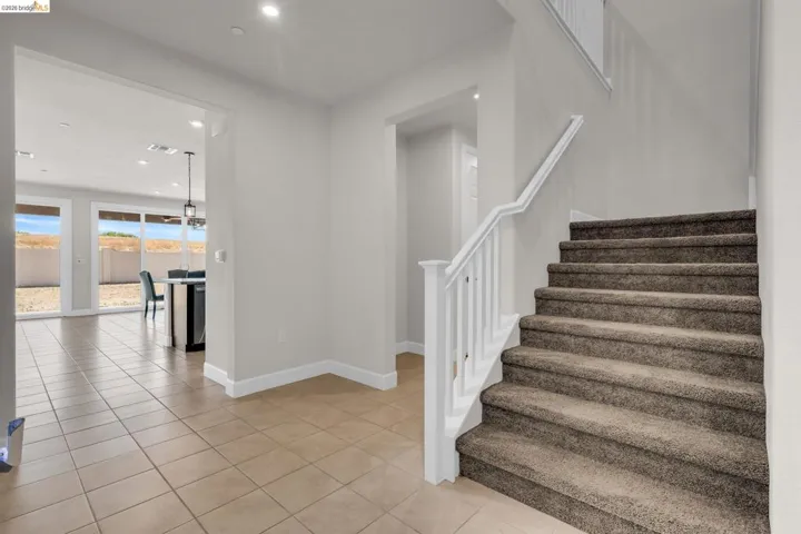 Foyer featuring neutral-toned tile flooring, recessed ceiling lighting, and a carpeted staircase with white railings