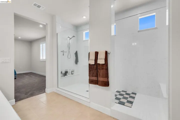 Spacious bathroom featuring a glass-enclosed shower with a built-in bench, two high windows, and recessed lighting