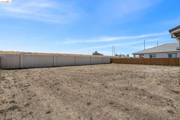 Expansive backyard space featuring a concrete privacy wall, wood fencing, and a clear sky backdrop