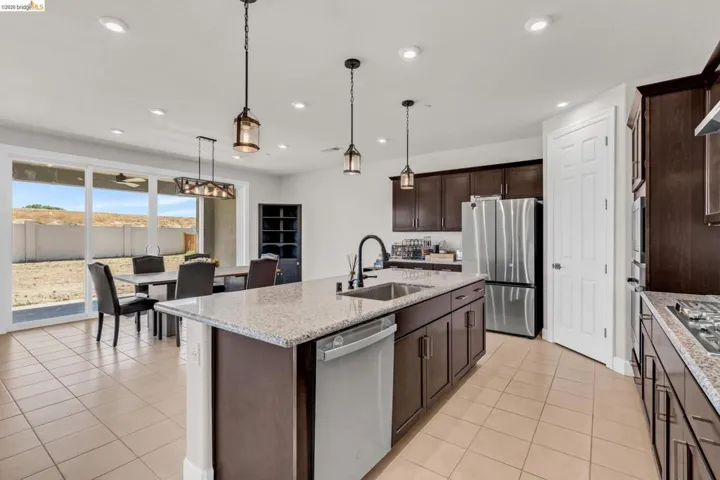 Spacious kitchen featuring a large island with sink, dark wood-finish cabinetry, stainless steel appliances, and light-toned tile flooring