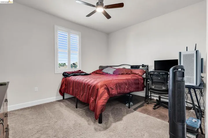 Carpeted interior space featuring a ceiling fan with integrated lighting, a window with plantation shutters, and light-toned walls