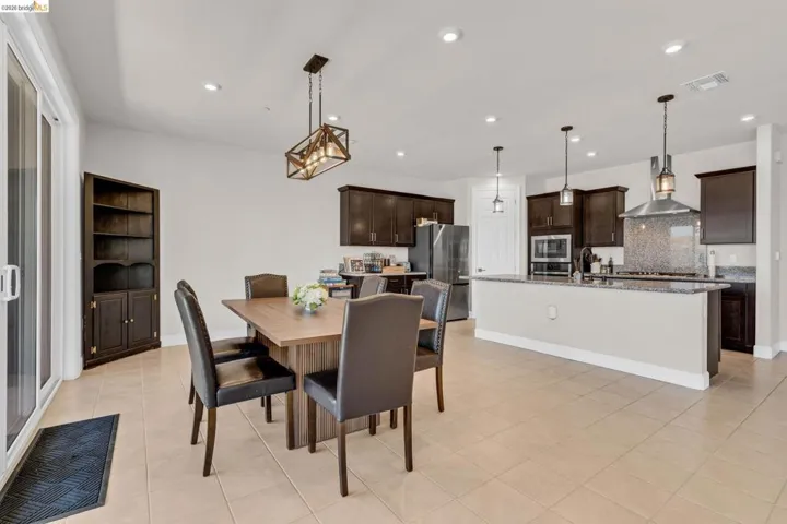 Open-concept living space featuring neutral tile flooring, recessed lighting, a modern chandelier, and a built-in dark wood bookcase