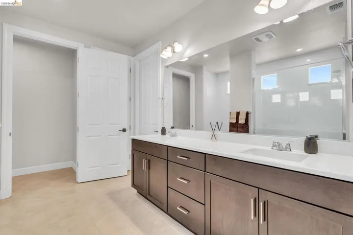 Bathroom vanity featuring dual sinks with integrated white countertops, dark wood-finish cabinetry, and a full-width mirror