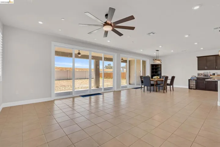 Expansive living area featuring large sliding glass doors, neutral tile flooring, recessed lighting, and a modern ceiling fan