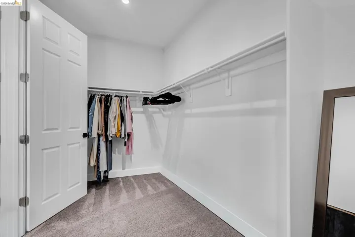 Spacious walk-in closet featuring light gray carpet flooring, white walls, and built-in white wire shelving and hanging rods