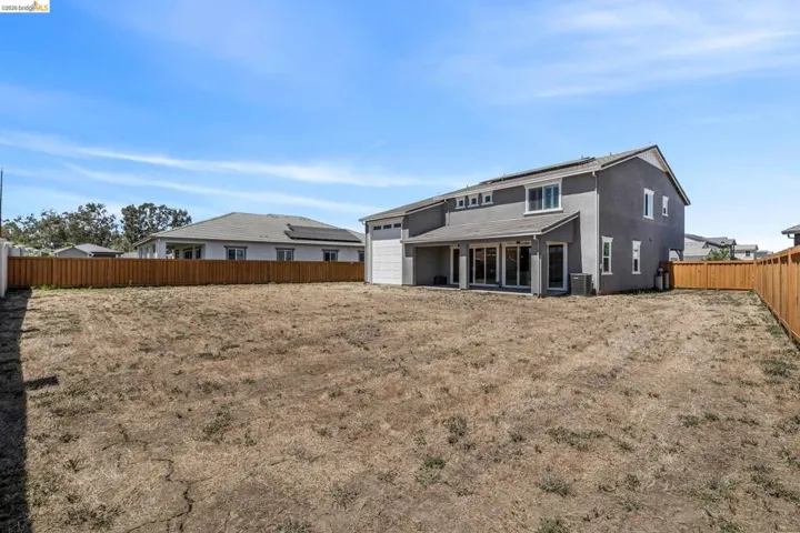 Expansive rear yard featuring a privacy fence, covered patio, and stucco exterior