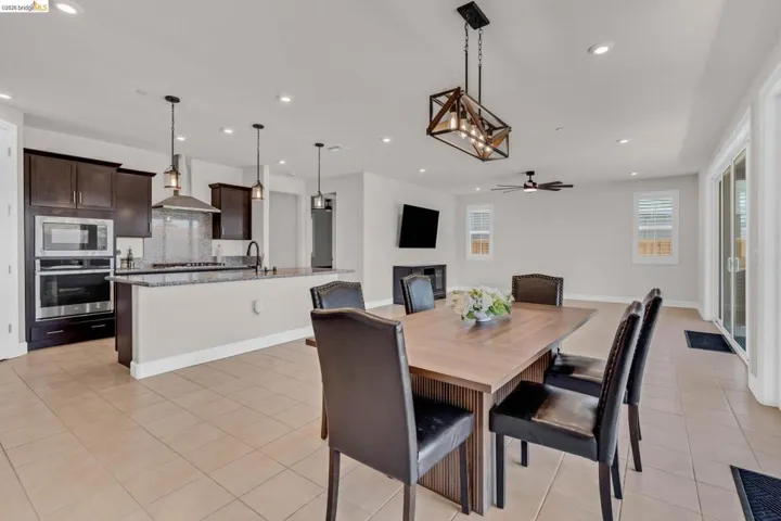 Open-concept living space featuring a central dining area, a kitchen island with pendant lighting, dark wood-finish cabinetry, a built-in oven and microwave, and large sliding glass doors