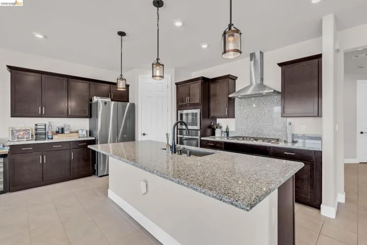 Kitchen featuring a large island with an undermount sink, granite countertops with a matching backsplash, stainless steel appliances, and dark wood​​‌​​​​‌​​‌‌​​‌​​​‌‌​​​‌​​‌‌​​‌‌​​‌‌​​​​ cabinetry