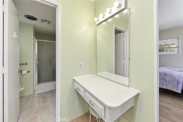 Another view of the vanity, 3/4 bath, and primary bedroom.