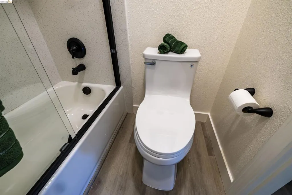 Bathroom featuring a white tub with black fixtures and a glass shower enclosure, a white toilet, and wood-finish flooring