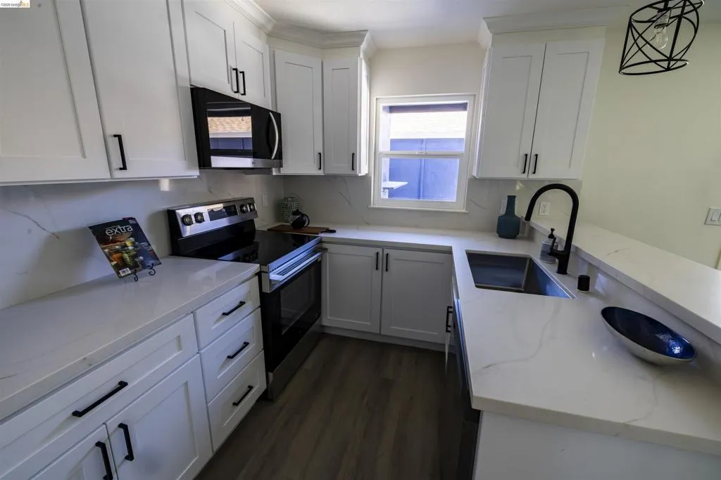 Modern kitchen featuring white shaker-style cabinetry, dark hardware, and light-toned countertops with subtle veining