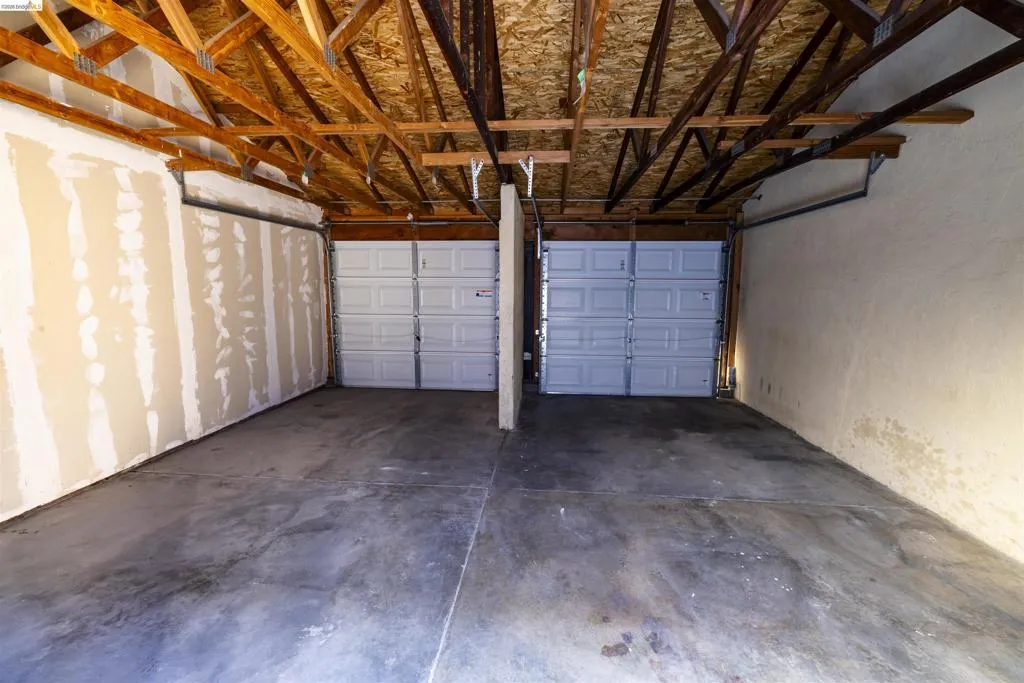 Two-car garage featuring exposed wood ceiling trusses and concrete flooring