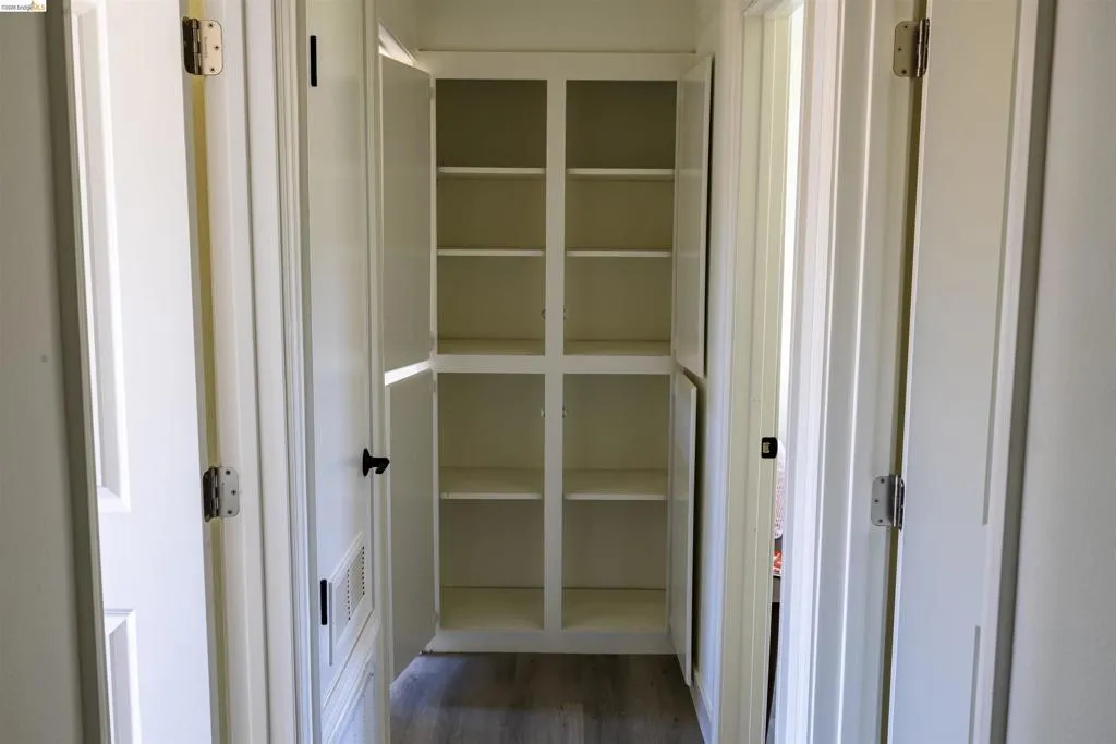 Hallway featuring built-in white cabinetry with multiple shelves, wood-finish flooring, and white paneled doors with black hardware