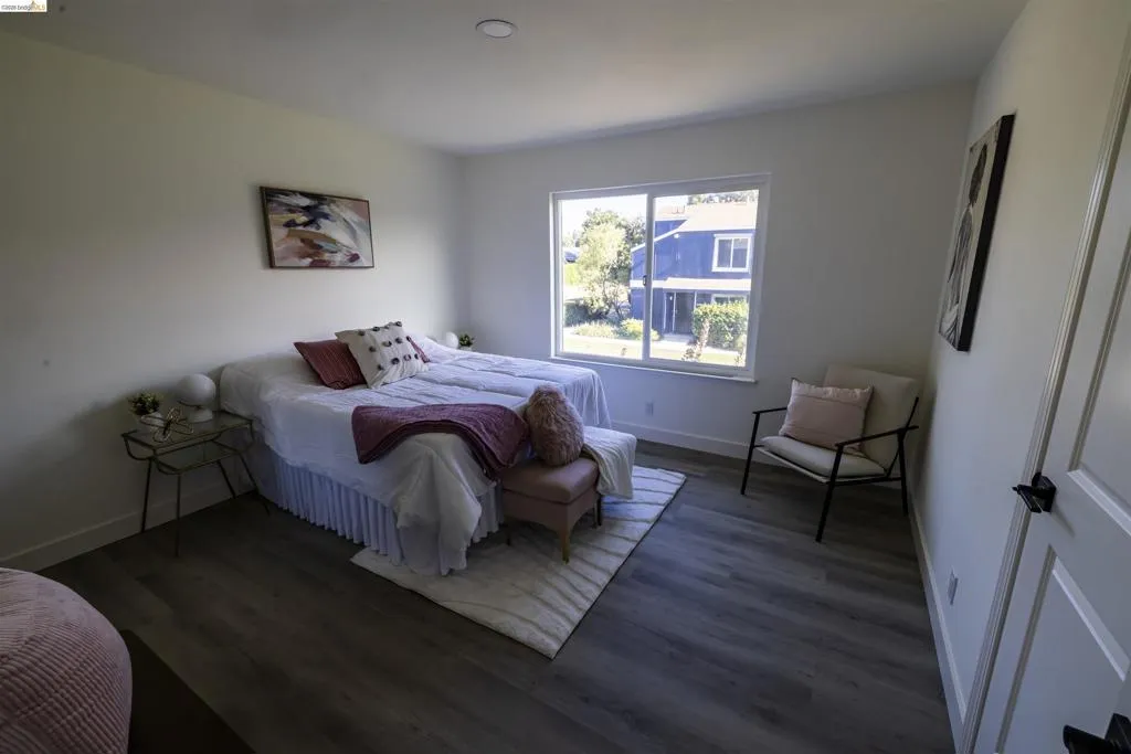 Spacious room featuring wood-finish flooring, a large window offering exterior views, recessed ceiling lighting, and a white paneled door with black hardware