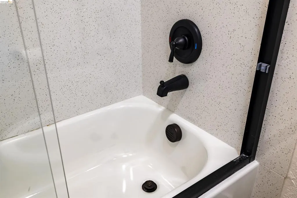 Bathtub featuring matte black fixtures, integrated shower controls, and a clear glass shower panel with a black frame