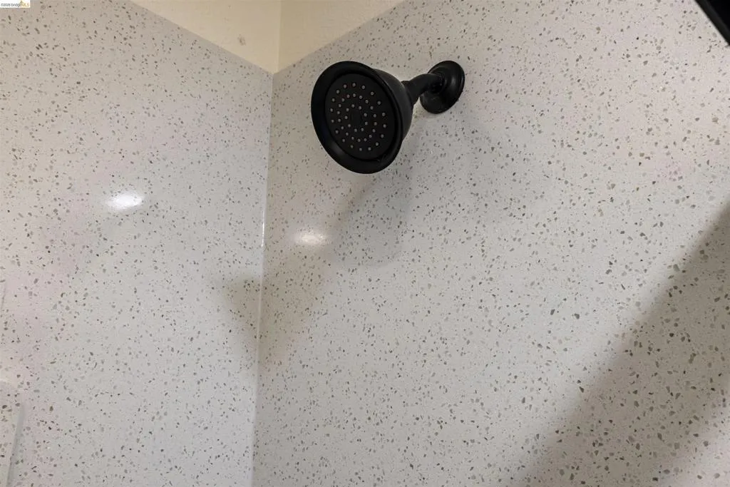 Shower featuring a matte black fixture against a white speckled wall