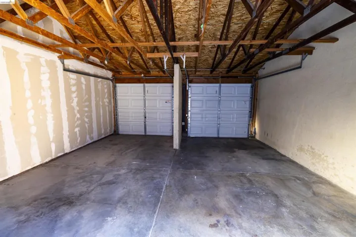 Two-car garage featuring exposed wood ceiling trusses and concrete flooring