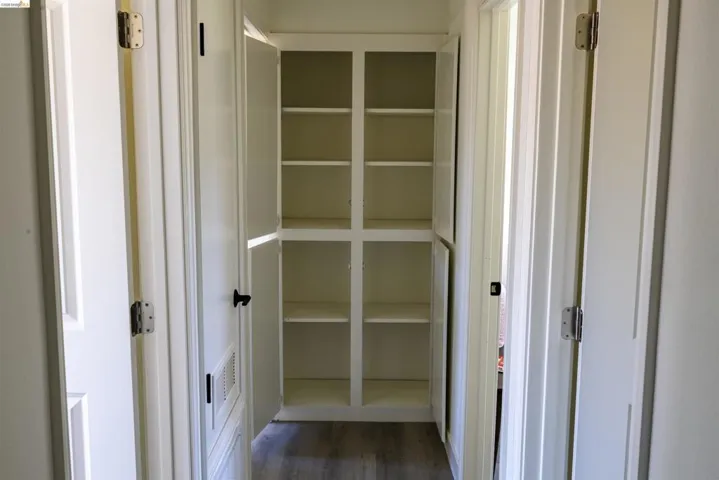 Hallway featuring built-in white cabinetry with multiple shelves, wood-finish flooring, and white paneled doors with black hardware