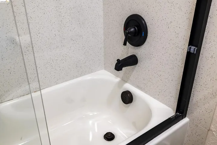 Bathtub featuring matte black fixtures, integrated shower controls, and a clear glass shower panel with a black frame