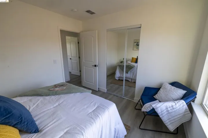 Bedroom featuring light-tone wood-finish flooring, a sliding mirrored closet door, and a white interior door with black hardware