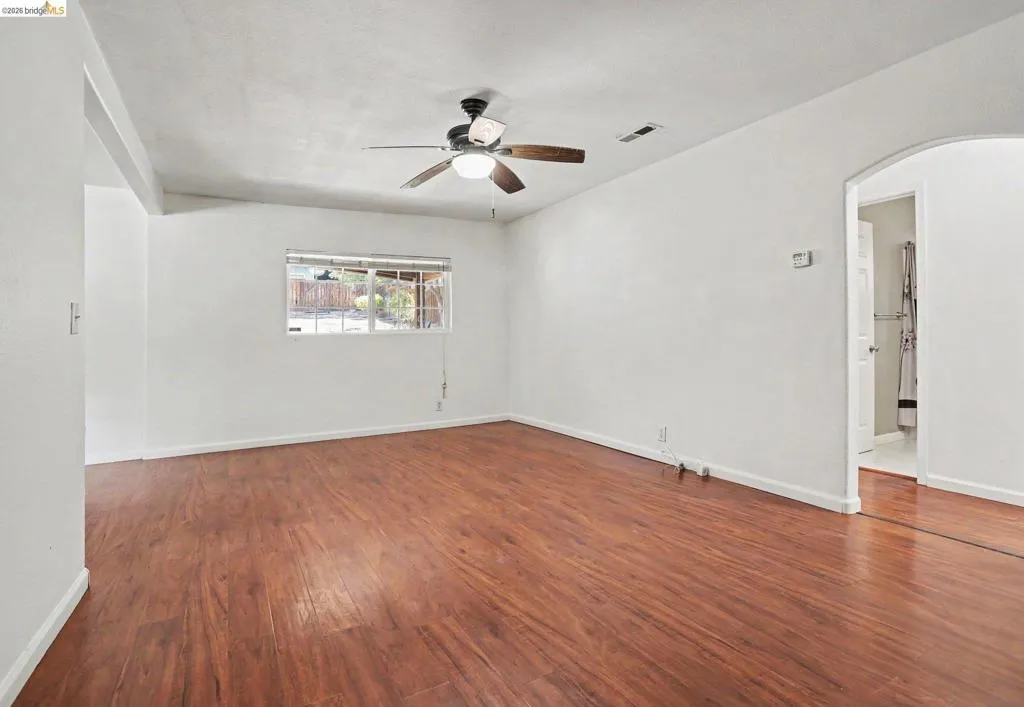 Wood-finish flooring, white walls, ceiling fan with integrated lighting, and an arched doorway
