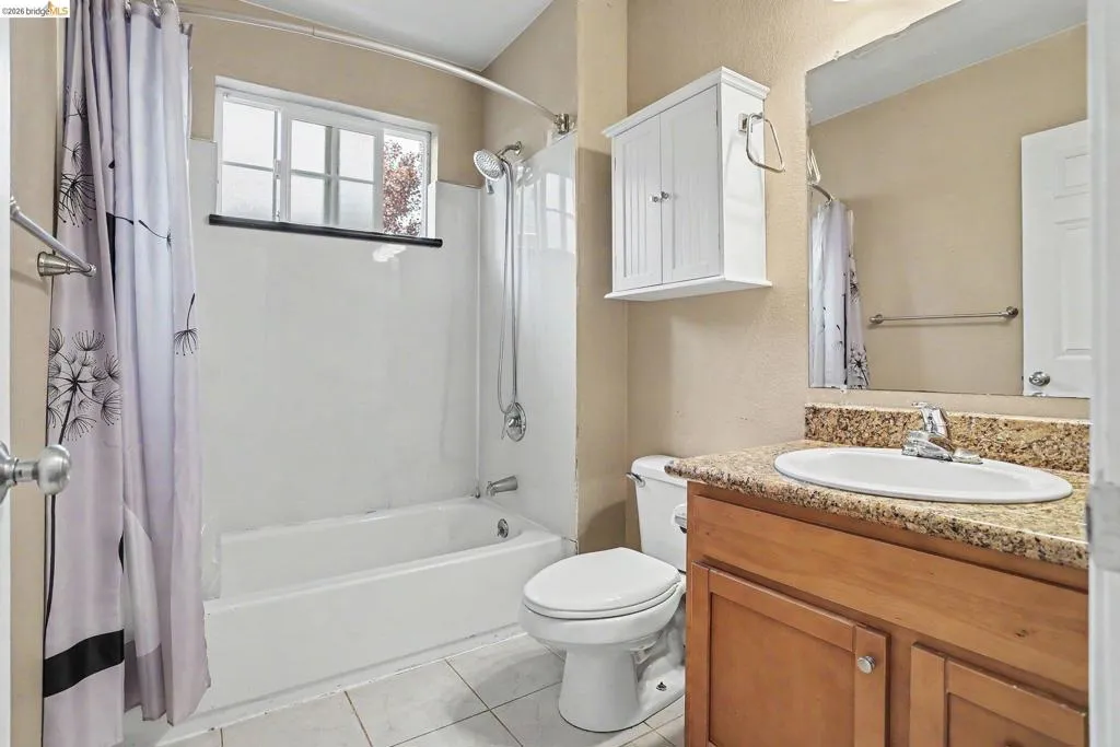 Bathroom featuring a white tub/shower combination with a frosted window, a light wood-finish vanity with a speckled countertop, an undermount sink, and a wall-mounted medicine cabinet