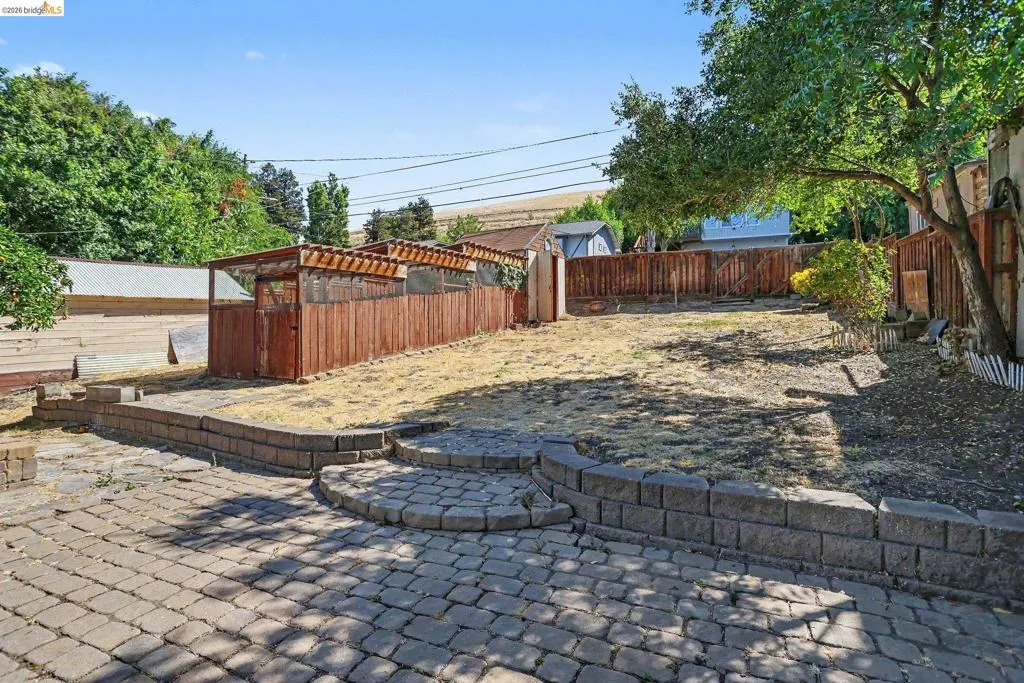 Spacious backyard with paver patio, terraced retaining walls, and a large wooden structure