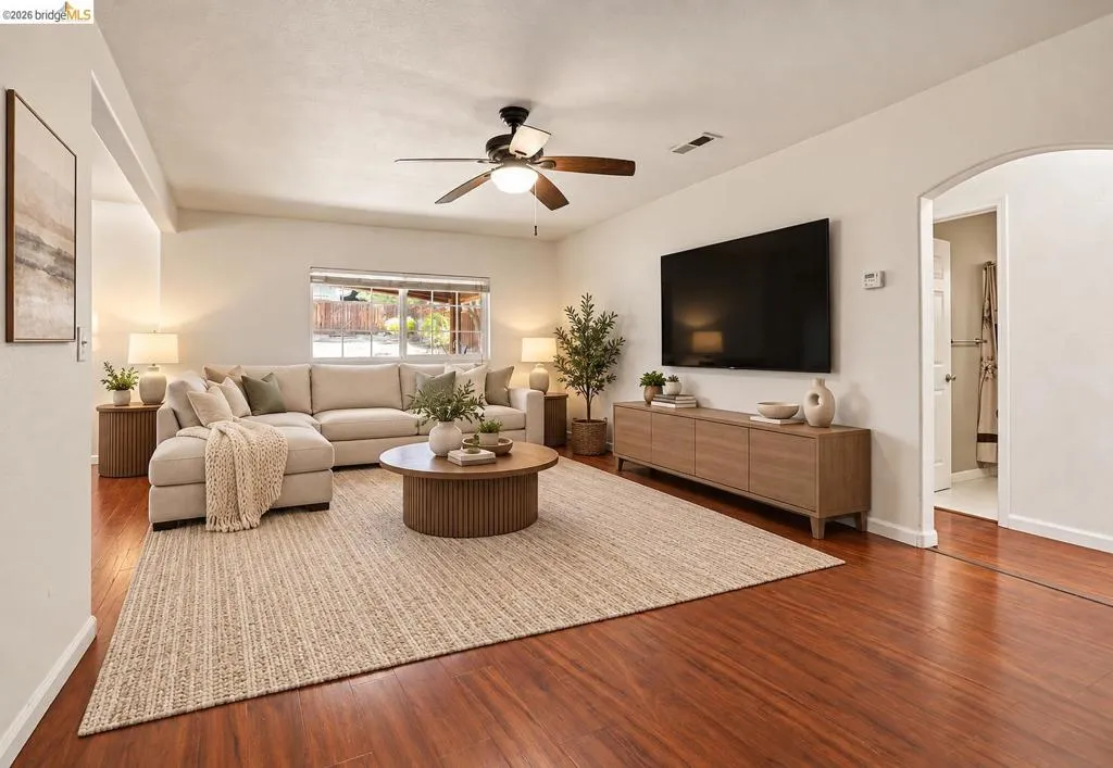 Wood-finish flooring throughout, featuring a ceiling fan, a window, and an arched doorway