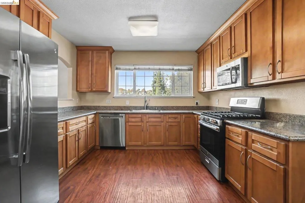 Kitchen featuring wood-finish flooring, ample cabinetry, stainless steel appliances, and stone countertops