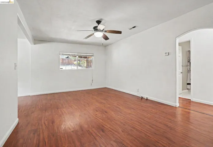 Wood-finish flooring, white walls, ceiling fan with integrated lighting, and an arched doorway