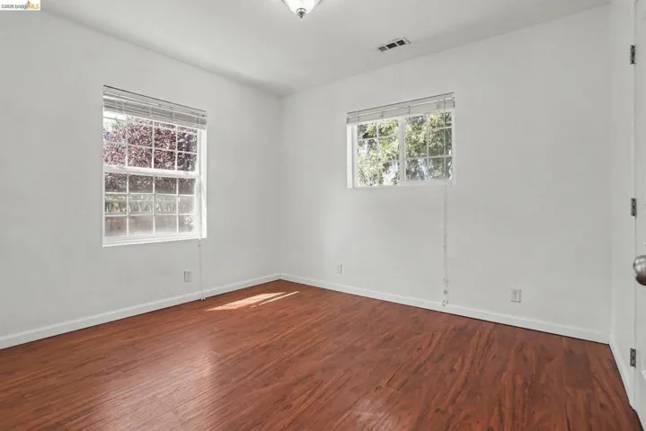 Bright room featuring wood-finish flooring, white walls, and two windows with blinds