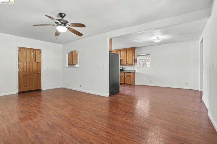 Spacious living area featuring wood-finish flooring, a ceiling fan with integrated lighting, and an arched pass-through to the kitchen