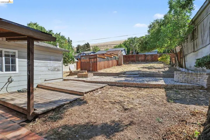 Tiered backyard featuring a wood deck, brick paver patio areas, stacked stone retaining walls, and perimeter fencing