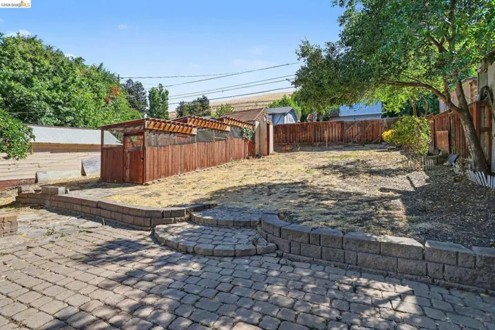 Spacious backyard with paver patio, terraced retaining walls, and a large wooden structure