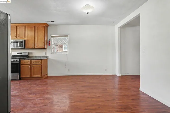 Open-concept living area featuring wood-finish flooring, recessed lighting, and a kitchen with wood cabinetry, stainless steel appliances, and a granite-style countertop