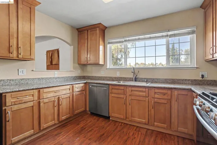 Kitchen featuring wood-finish flooring, light wood cabinetry, stone countertops, and a stainless steel dishwasher