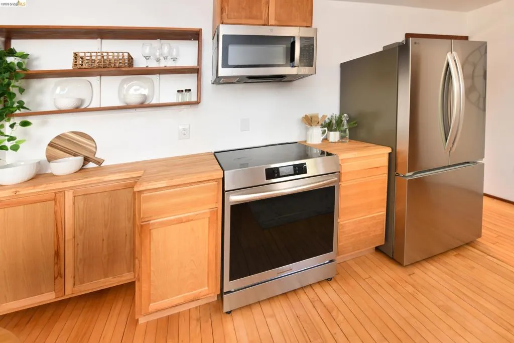 Kitchen featuring stainless steel appliances, wood-finish flooring, light wood cabinetry, butcher block countertops, and open shelving