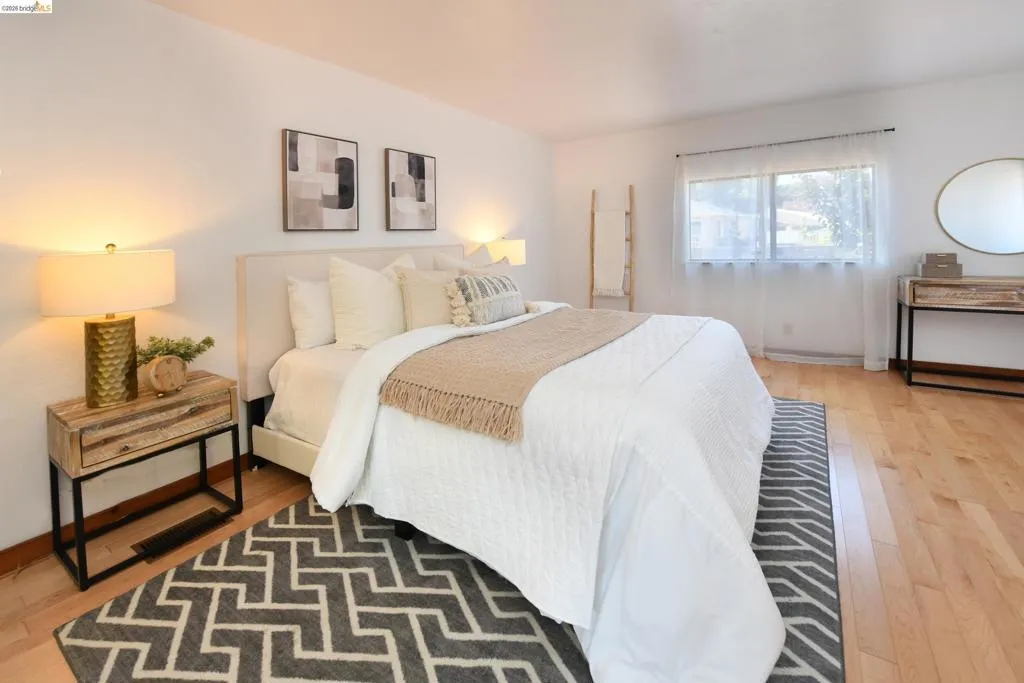 Bright room featuring wood-finish flooring, a large window with sheer curtains, and a light-colored accent wall
