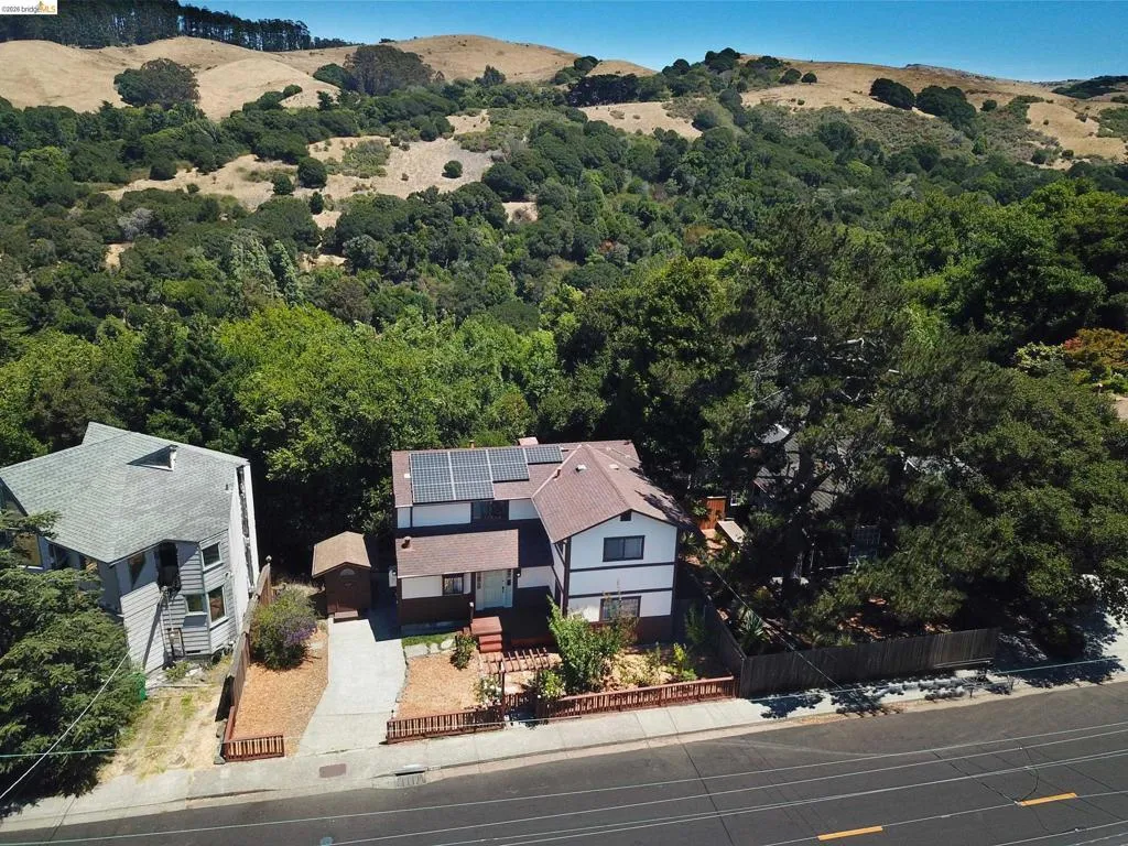 Two-story residence featuring a brown shingle roof with solar panels, a light-colored stucco exterior with dark trim, and a concrete driveway