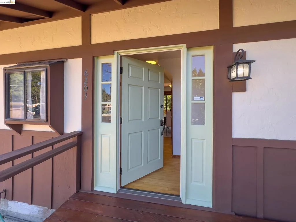 Front entry featuring a light green paneled door, sidelight windows, and a wood-finish porch floor