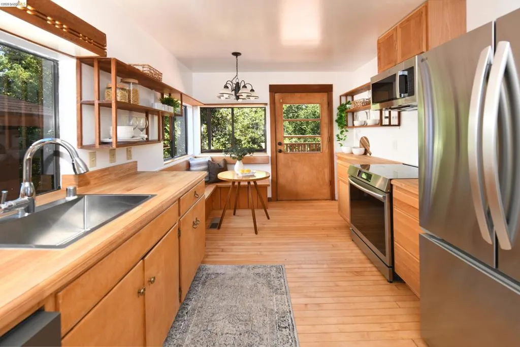Galley kitchen featuring wood-finish flooring, wood cabinetry, stainless steel appliances, and wood countertops