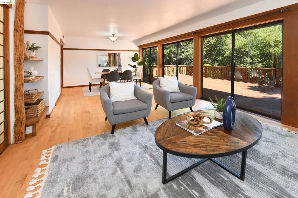 Open-concept living area featuring wood-finish flooring, a dining space with a ceiling light fixture, and multiple large sliding glass doors providing access to an exterior wood deck