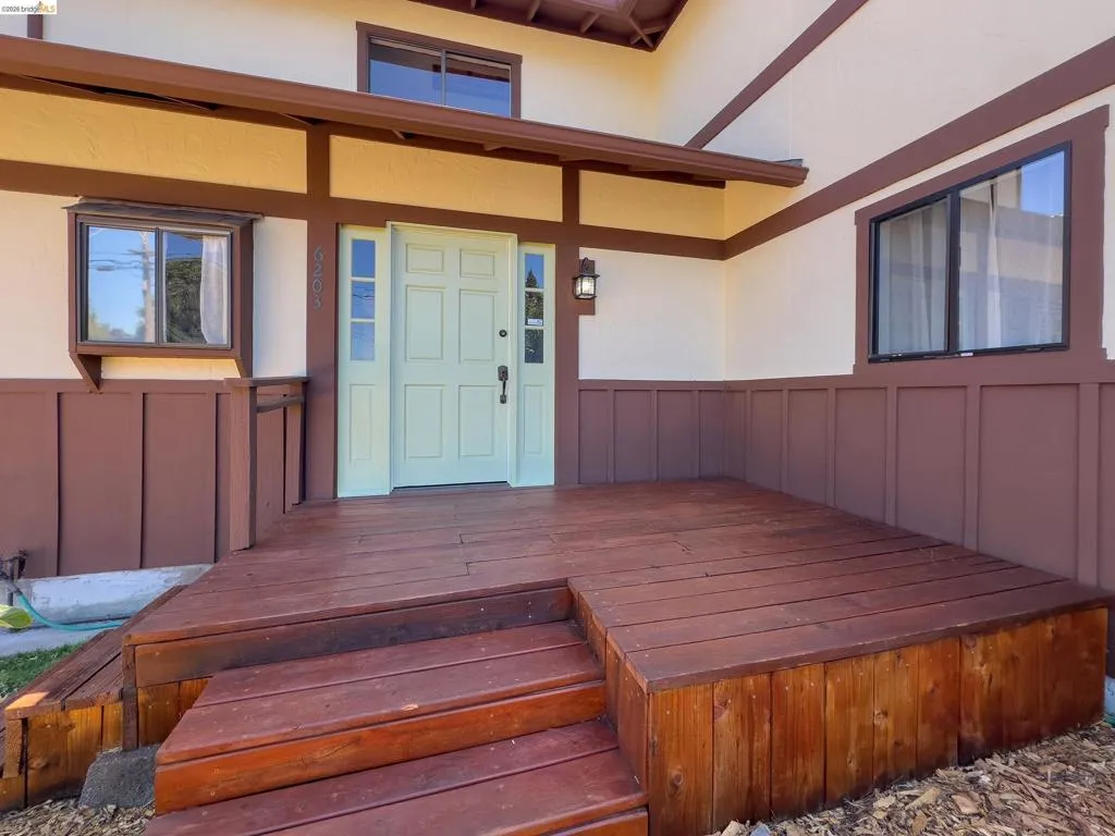 Expansive wood-finish deck with multiple steps, featuring a light green entry door flanked by sidelights
