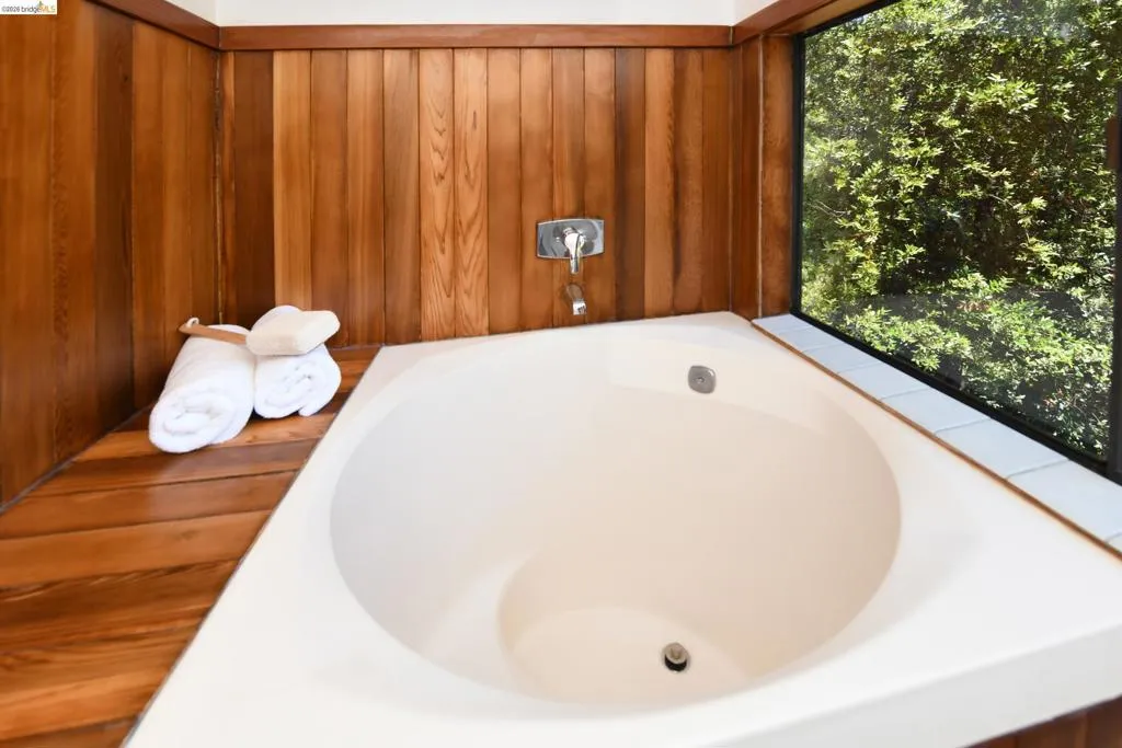 Built-in corner soaking tub with wood-finish paneling and a large picture window
