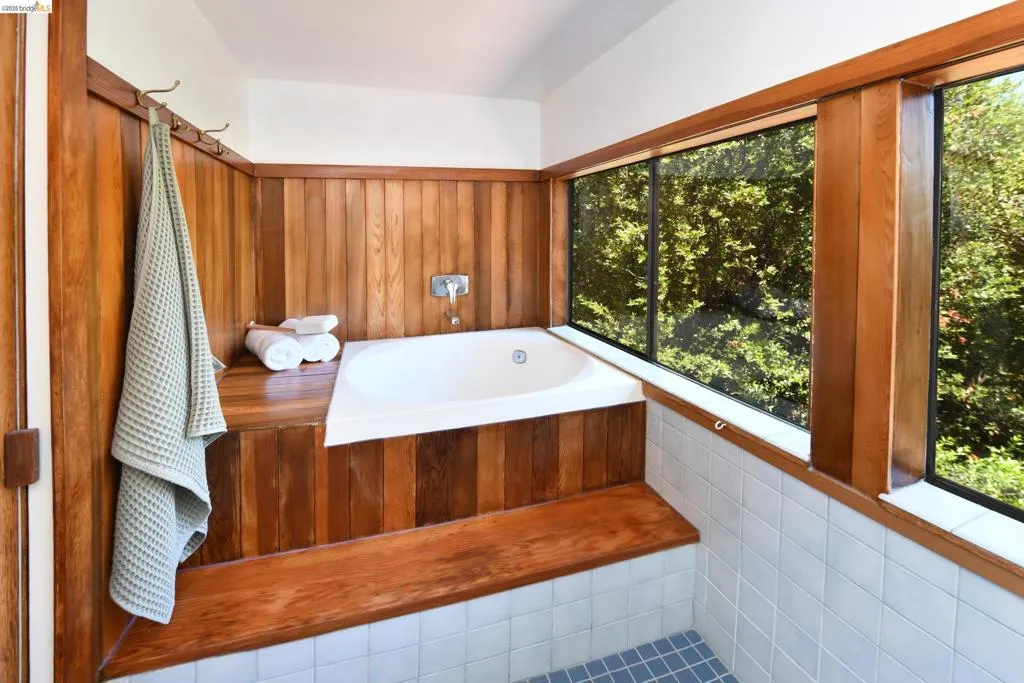 Built-in soaking tub with polished chrome fixtures, surrounded by wood-paneled walls and a wood-finish bench